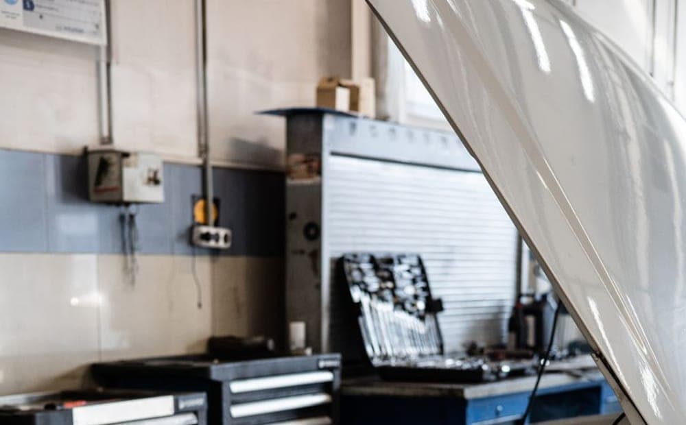 Carro com o capô aberto numa oficina organizada, com carrinhos de ferramenta ao fundo